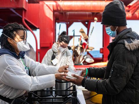 Une membre de l'équipage distribue un kit de nourriture à un rescapé sur le pont du bateau.