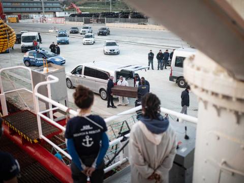 Des membres de l'équipage regardent depuis le pont du bateau un cercueil porté par les autorités italiennes. Il contient le corps d'un homme décédé sur une embarcation en détresse.